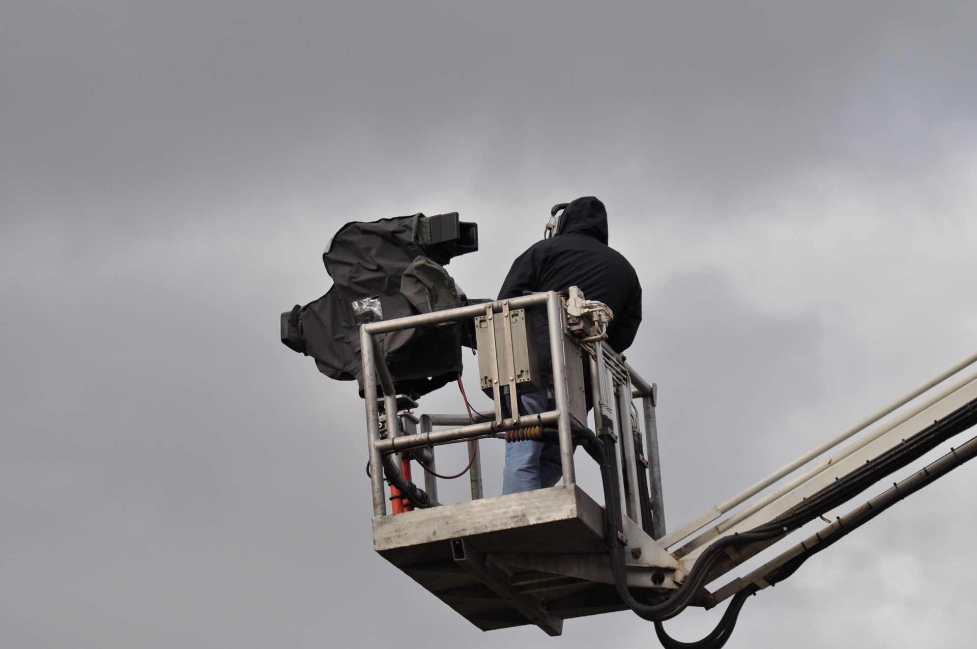 Kameramann mit Filmkamera auf Arbeitsbühne bei bewölktem Himmel.