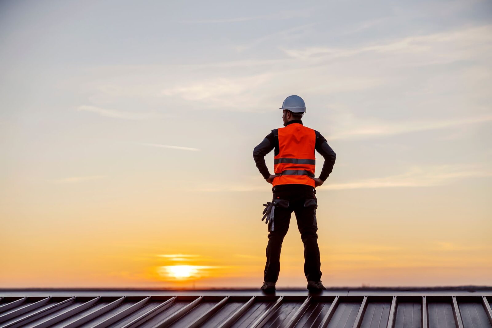 Arbeiter mit Warnweste steht auf Dach beim Sonnenuntergang.